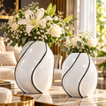 Deux vases blancs sculpturaux aux courbes arrondies et liseré noir, présentés avec des bouquets