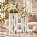 Deux vases décoratifs blancs au design sculptural et entrelacé, présentés avec des compositions florales