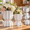 Duo de vases blancs à texture striée et pied sculpté, présentés avec des bouquets de fleurs